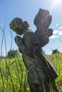 Praying stone Angel in a field of grass with blue sunny sky.