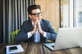 Praying for success. Front view of thoughtful young man holding hands on chin and looking at the laptop while sitting at his worki Royalty Free Stock Photo