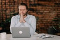 Praying for success. thoughtful young man holding hands on chin and looking at the laptop while sitting at his working Royalty Free Stock Photo