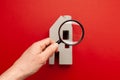 Pre-purchase property inspection. Miniature of the house and a magnifying glass in hand on a red background