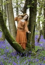 Woman with long red hair with pensive look standing on the bough of a tree above Blue Bells