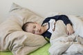 Pre-school sick boy with closed eyes lying in bed with a digital thermometer