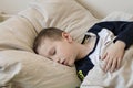 Pre-school sick boy with closed eyes lying in bed with a digital thermometer