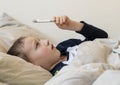 Pre-school sick boy in pyjama lying in bed and looking at digital thermometer