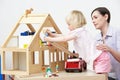 Pre-School Teacher And Pupil Playing With Wooden House