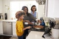 Pre-teen African American girl standing at the hob in the kitchen preparing food with her grandmother and mother, selective focus