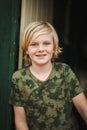 Pre-teen boy with long blonde hair smiling while wearing army print shirt Royalty Free Stock Photo