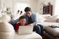 Pre-teen boy lying on sofa using laptop, dad sitting beside him, mum and sister in the background Royalty Free Stock Photo