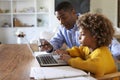 Pre teen girl African American girl using a laptop computer sitting at table in the dining room with her home tutor, selective fo