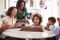 Pre teen girl blowing out the candles on birthday cake sitting at table in the kitchen with her three generation family, selective Royalty Free Stock Photo