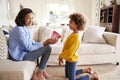 Pre-teen girl kneeling and giving her mother a homemade decorated plant pot, mum looking to camera, side view