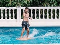 Pre-teens play in the pool by jumping on a small surfboard to keep their balance Royalty Free Stock Photo