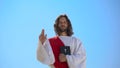 Preacher in robe showing hand of benediction, holding Bible, blessing christians