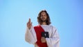 Preacher in robe showing hand of benediction, holding Bible, blessing Christians