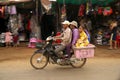 Panning of Four persons on motorbike passing Sra`aem Market in Preah Vihear province, Camb