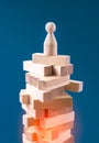 Precarious business situation concept with wooden human figurine standing on wooden blocks.