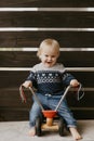 Precious Adorable Cute Little Blonde Baby Toddler Boy Kid Playing Outside on Wooden Toy Bicycle Scooter Mobile Smiling at the Came Royalty Free Stock Photo