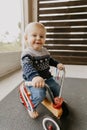 Precious Adorable Cute Little Blonde Baby Toddler Boy Kid Playing Outside on Wooden Toy Bicycle Scooter Mobile Smiling at the Came