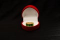 A precious golden ring with green stones in the heart-shaped box isolated on black background Royalty Free Stock Photo