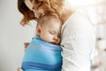 Precious little newborn boy having deep sleep at day on mother chest in blue baby sling. Mom kissing baby head and