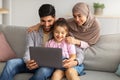 Precious time with family. Happy muslim parents and cute little girl using laptop together, watching photos or movie Royalty Free Stock Photo