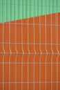 Prefabricated grating wire fence panel with blurred background of orange steel wall and green metal roof