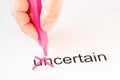 The prefix `un` of the word uncertain is crossed out with a pink pencil by a hand