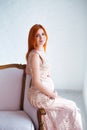 Pregnancy beauty. Beautiful elegant readhead pregnant woman in charming dress posing in tender home interior.