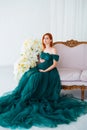 Pregnancy beauty. Beautiful elegant readhead pregnant woman in green dress posing in tender home interior.