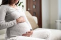 Pregnancy concept, pregnant woman touching belly with hands sitting on couch Royalty Free Stock Photo