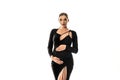 Pregnancy concept. Woman posing in white studio background wearing black dress, holding her pregnant belly, looking at the camera Royalty Free Stock Photo