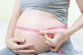 Pregnancy, gynecology, nutrition, health care and people concept - Pregnant woman using centimeter tape measuring her tummy to