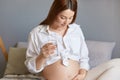 Pregnancy. Healthy lifestyle. Health care. Responsible pregnant woman with bare belly wearing white clothing sitting in bed Royalty Free Stock Photo