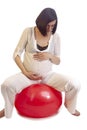Pregnancy Ideas. Portrait of One Caucasian Brunette Woman in White Clothing Sitting on Big Fitball With Hands Holding Belly Over Royalty Free Stock Photo