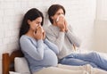 Pregnant couple feeling sick, sitting on bed and blowing noses Royalty Free Stock Photo