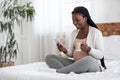 Pregnancy Leisure. Black Expecting Lady Relaxing On Bed With Smartphone And Tea