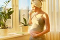 Pregnant young woman with bath towel on head with cup of tea looking out window Royalty Free Stock Photo