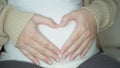 pregnancy love people and expectation concept - happy pregnant woman making heart gesture over holidays lights background.