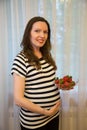 Pregnancy, motherhood, the concept of waiting-close - up of a happy pregnant woman with a big belly in a window with strawberries Royalty Free Stock Photo