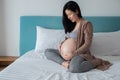 Pregnancy, motherhood and expectation concept - smiling asian  pregnant woman touching big belly on bed Royalty Free Stock Photo