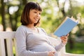 Happy pregnant asian woman reading book at park Royalty Free Stock Photo