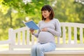 Happy pregnant asian woman reading book at park Royalty Free Stock Photo