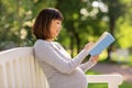 Happy pregnant asian woman reading book at park Royalty Free Stock Photo