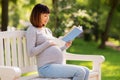 Happy pregnant asian woman reading book at park Royalty Free Stock Photo