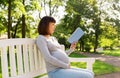 Happy pregnant asian woman reading book at park Royalty Free Stock Photo