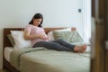 Pregnancy, people rest and expectation concept - Asian smiling happy pregnant woman sitting in bed and touching her belly at home Royalty Free Stock Photo