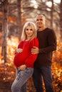 Pregnancy. Pregnant couple in white outfits enjoying in autumn forest park. Loving man hugging his beautiful wife. Parenthood