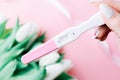 Pregnancy test couple. Positive woman pregnant test in hands with pink silk ribbon on tulips flower pink background. New Royalty Free Stock Photo