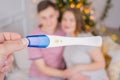 Pregnancy test in hands on background of defocused smiling young couple at home, Christmas time