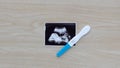 Pregnancy test showing a positive result and ultrasound picture of baby isolated on wooden background. Result of ultrasound pictur Royalty Free Stock Photo